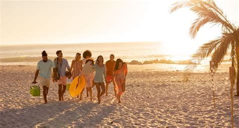 Group walking on a sandy beach at sunset, carrying surfboards near the shoreline.