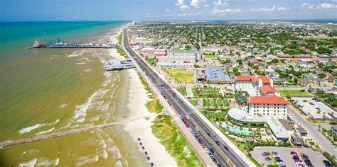Aerial view of a coastal city with a beach, turquoise water, highway, and colorful buildings under a clear sky