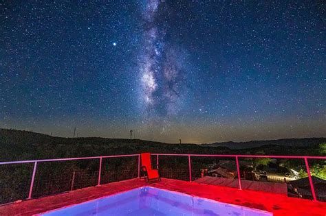 Starry night sky with the Milky Way above a lit rooftop pool and distant dark horizon