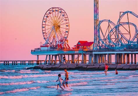 Amusement pier at sunset with Ferris wheel, roller coaster, and people wading in the ocean