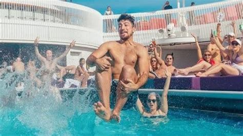 Man splashes into a pool while a crowd cheers from the deck behind him.