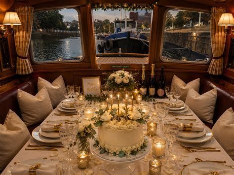 Elegant candlelit dinner table in a wood-paneled boat cabin, set with flowers and wine by the water