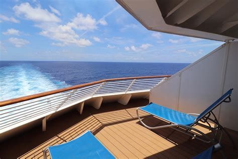 Cruise ship deck with blue lounge chairs overlooking the ocean and foamy wake at sunset