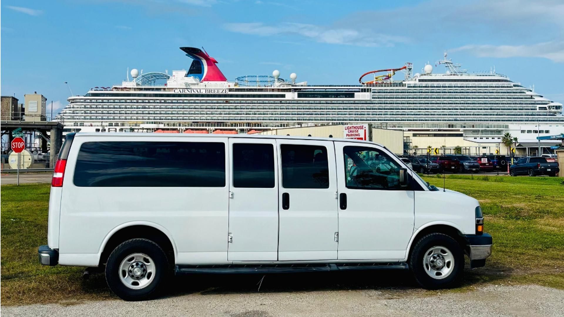 White van parked in front of a large cruise ship at a waterfront terminal