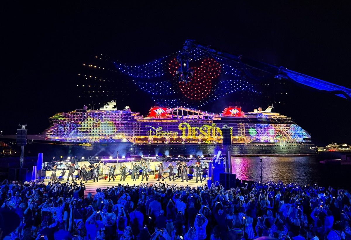 Nighttime cruise ship lit in blue and purple, with a large crowd watching a stage performance on deck