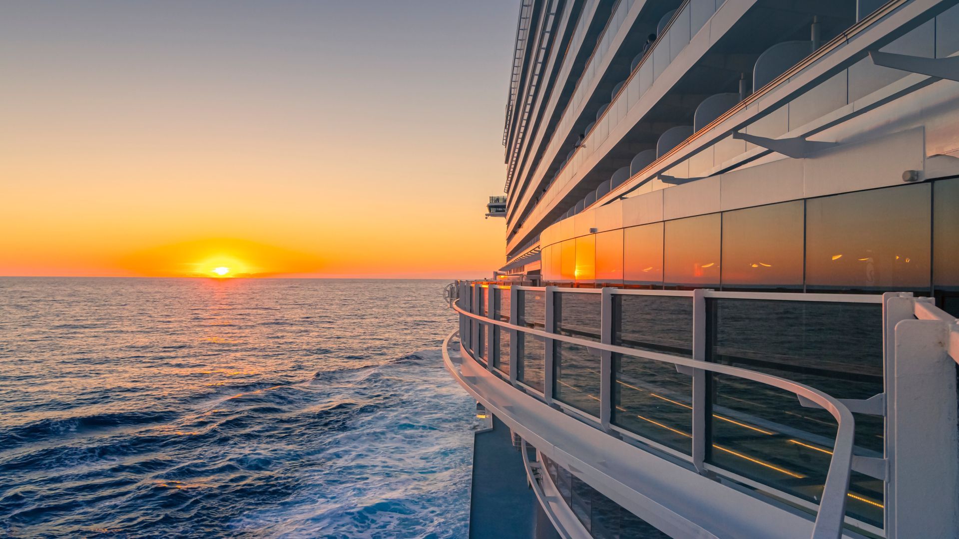 Sunset over the ocean beside a cruise ship deck with orange reflections on the windows