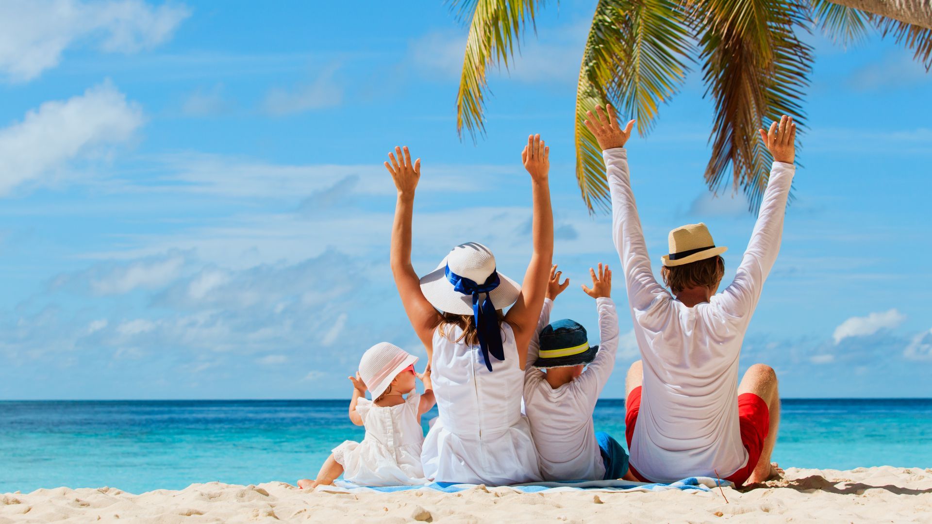 A family is sitting on the beach with their arms in the air.