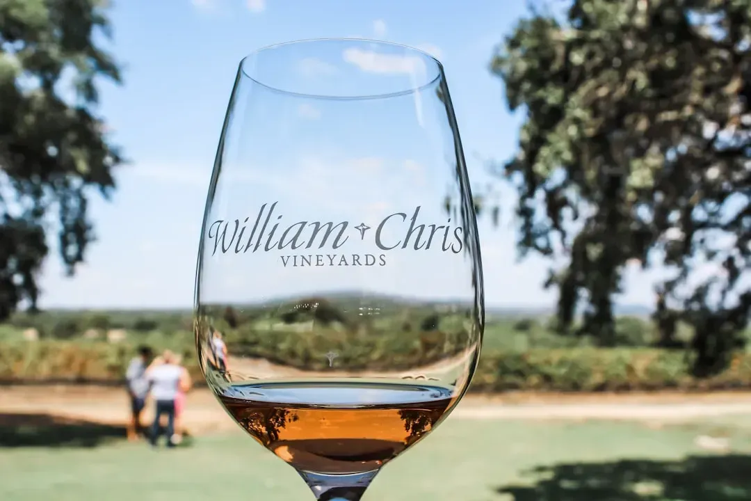 A glass of wine is sitting on a table in a field.