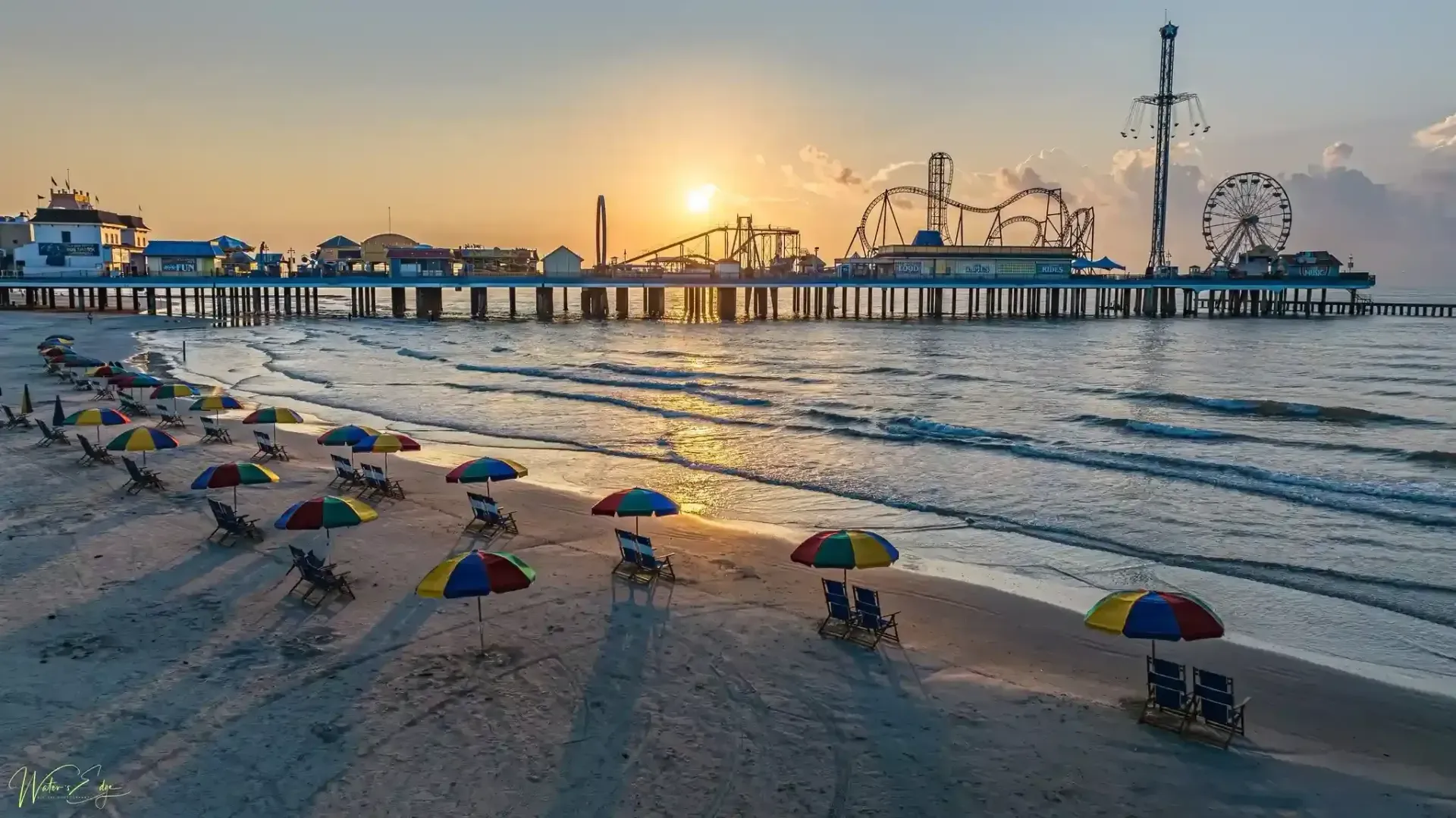 A beach with chairs and umbrellas at sunset with a pier in the background.