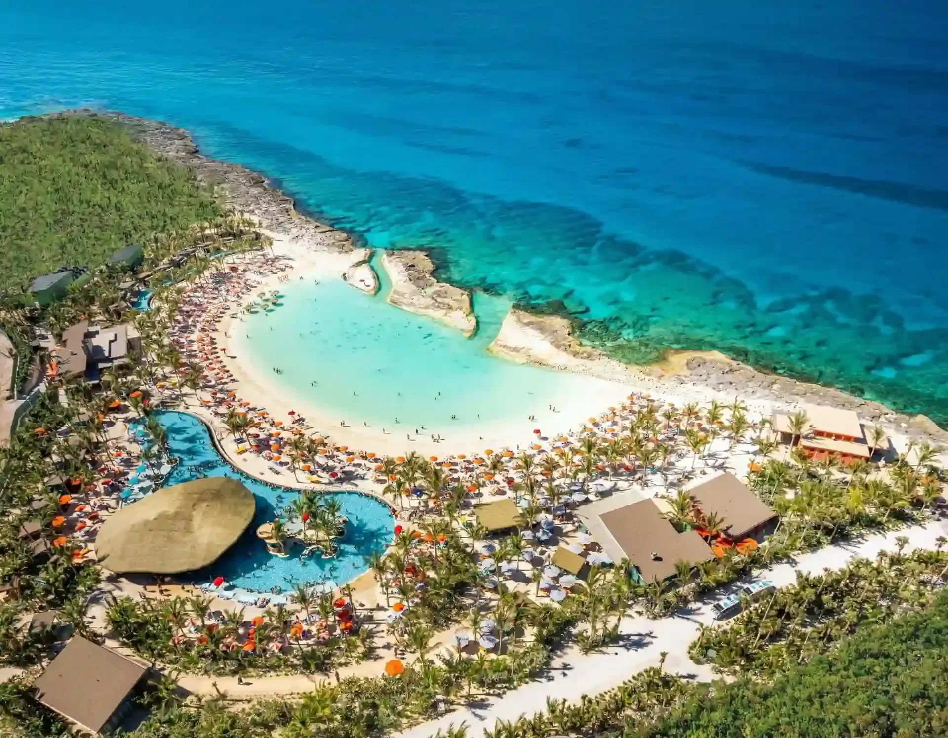 An aerial view of a tropical beach resort with a large pool surrounded by palm trees.