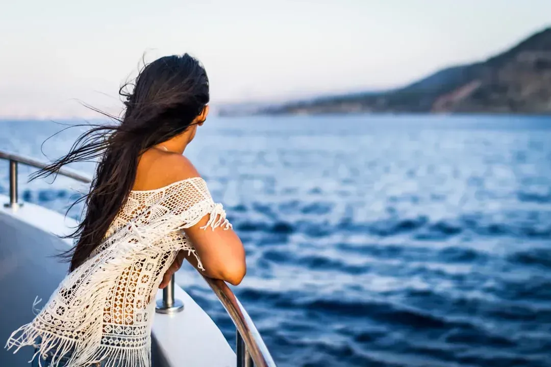 A woman is standing on the side of a boat looking at the ocean.