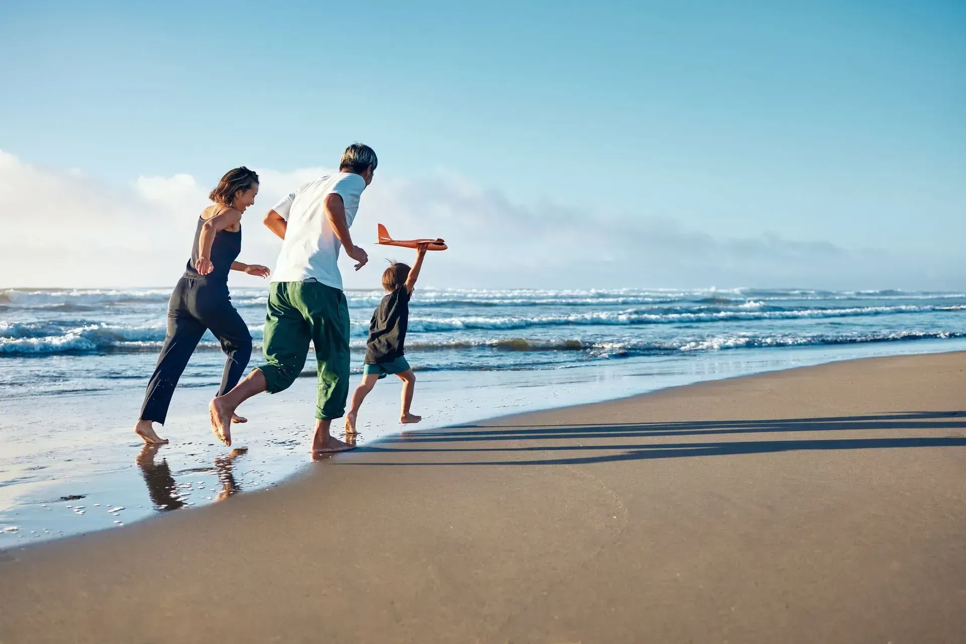 A family is playing with a toy airplane on the beach.