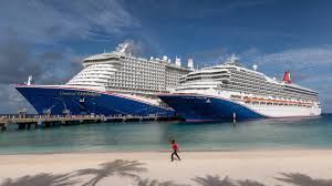 Two large cruise ships docked by a tropical beach, with a person walking on the sand.