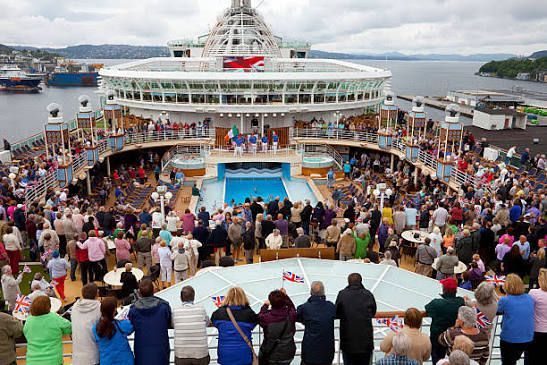 Crowded cruise ship deck party around a blue pool with passengers watching and dancing