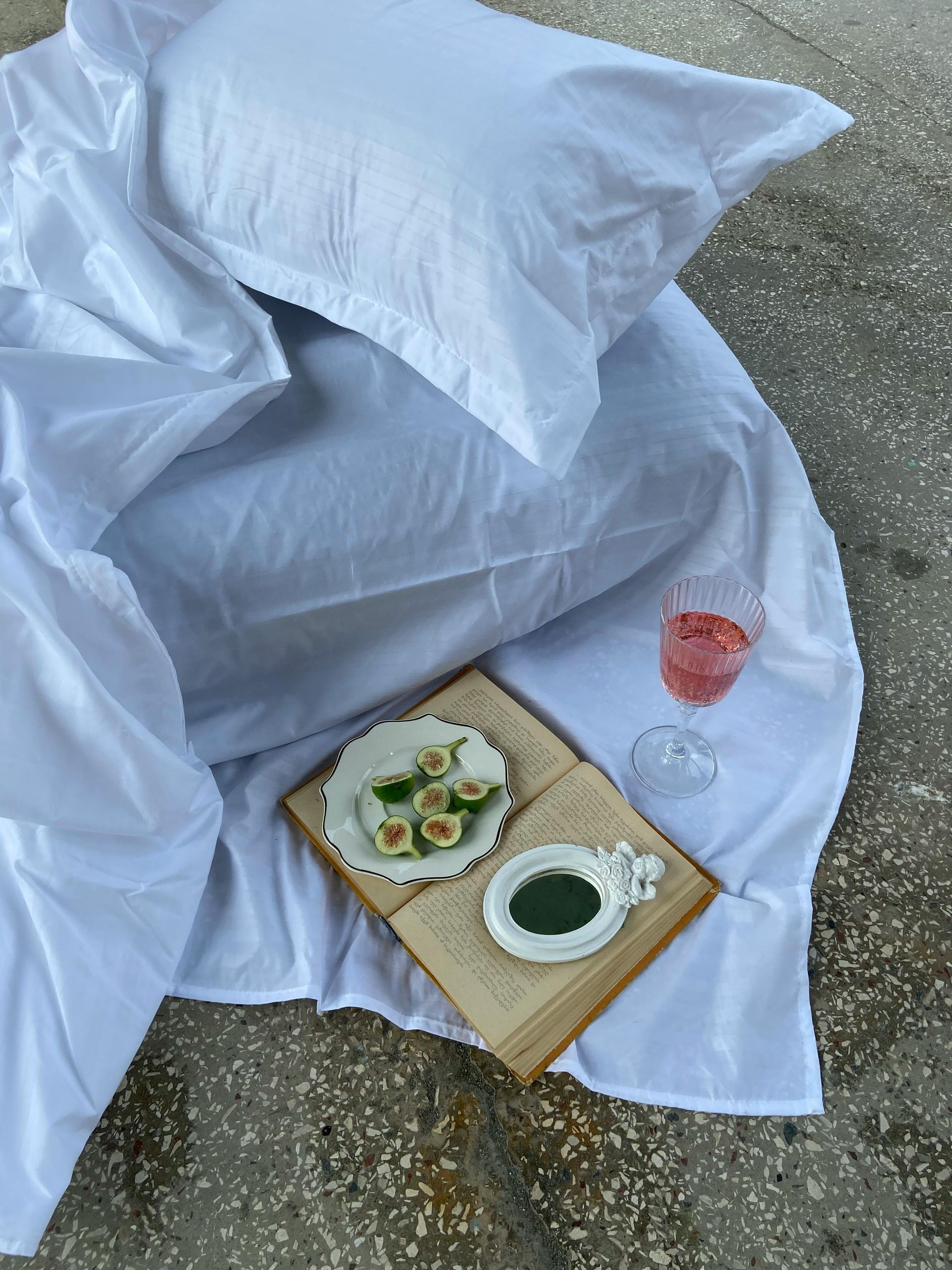A bed with white sheets and pillows and a plate of food and a glass of wine