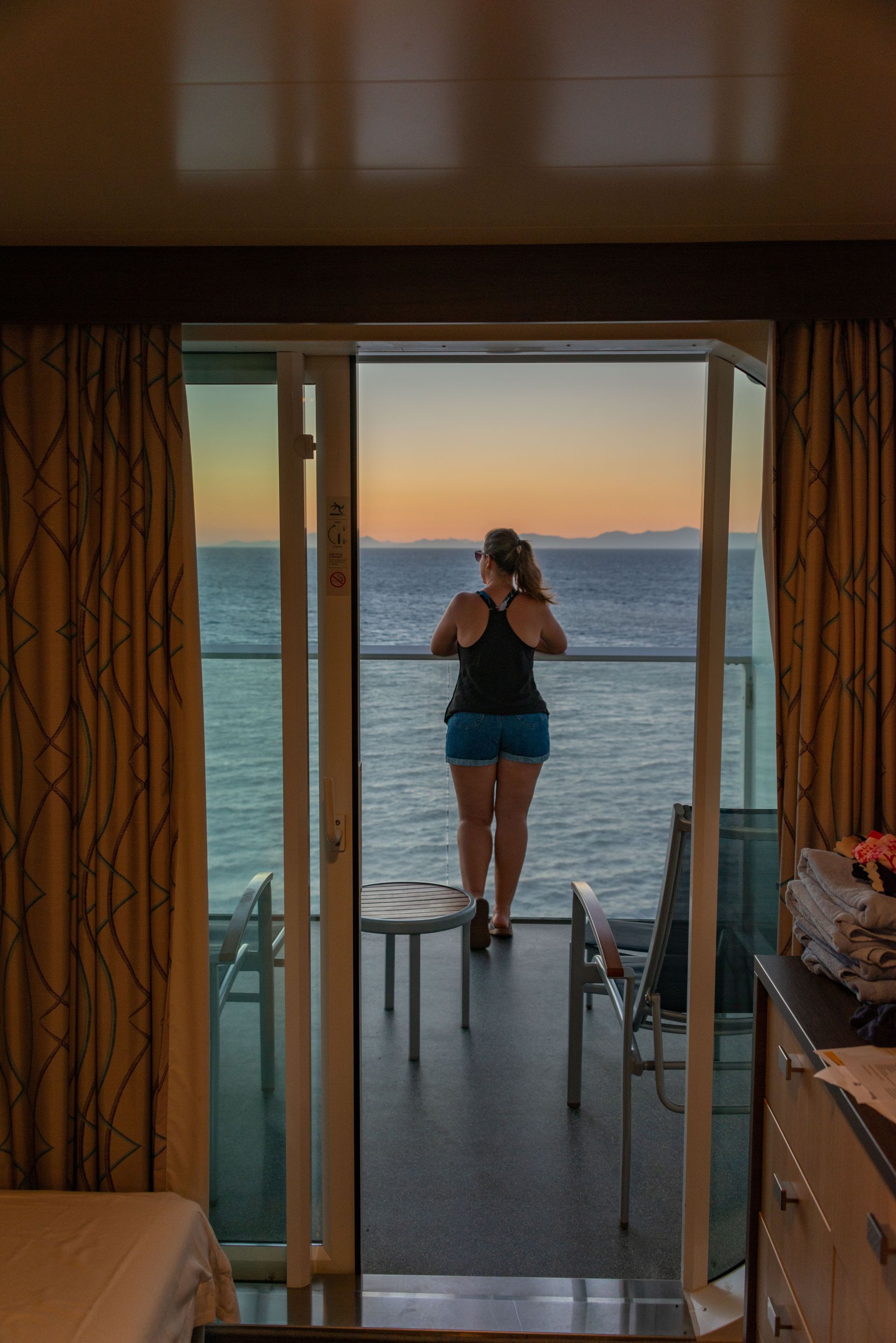 Person stands on a balcony at sunset, looking out over the ocean.