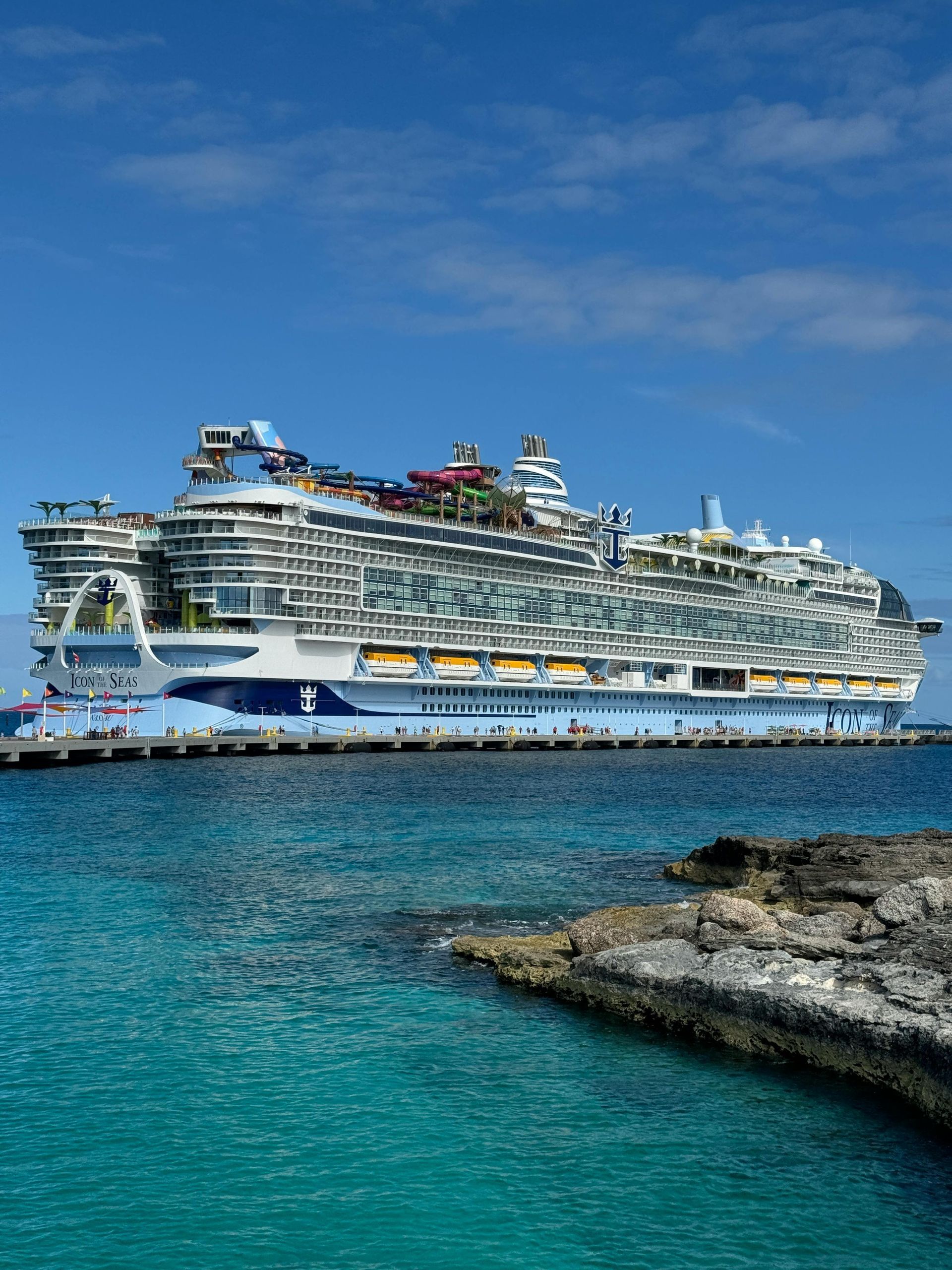 Large white cruise ship on turquoise water near rocky shoreline under a clear blue sky