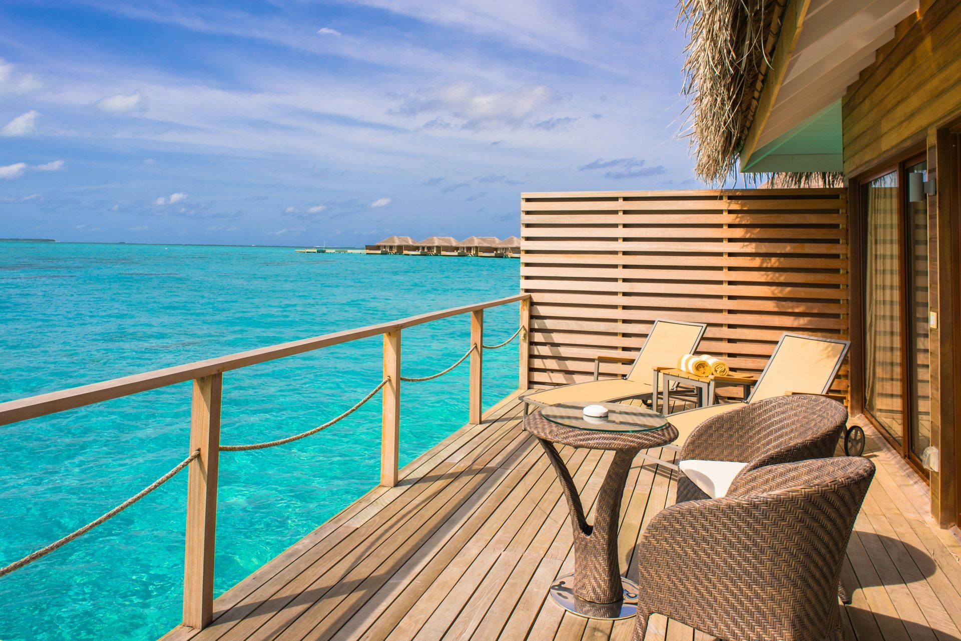 A wooden deck with chairs and a table overlooking the ocean.