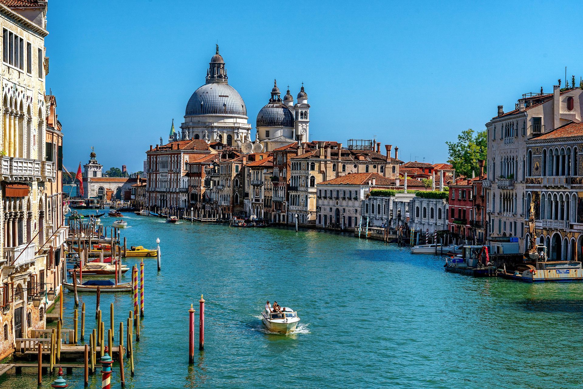 Venice canal with a gondola, colorful buildings, and a large domed basilica under a blue sky