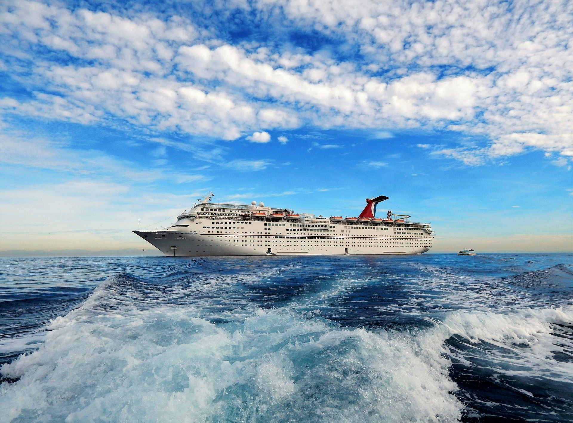 Large white cruise ship sailing on choppy blue ocean under a cloudy sky