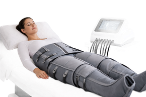 Persona sdraiata su un letto con indosso una tuta grigia per terapia compressiva, con un'unità di controllo nelle vicinanze.