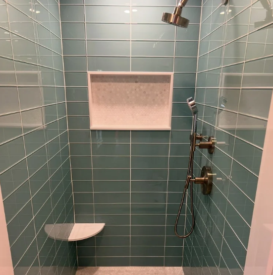 Small teal tiled shower stall with wall niche, showerhead, controls, and a built-in corner seat.