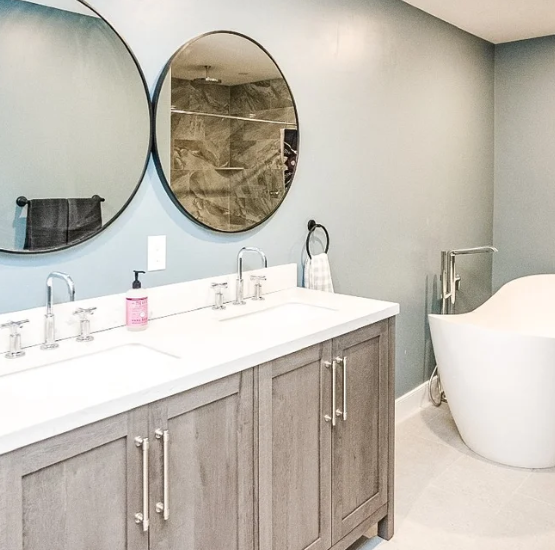 Bright bathroom with double vanity, round mirrors, and a freestanding tub beside a tiled shower.
