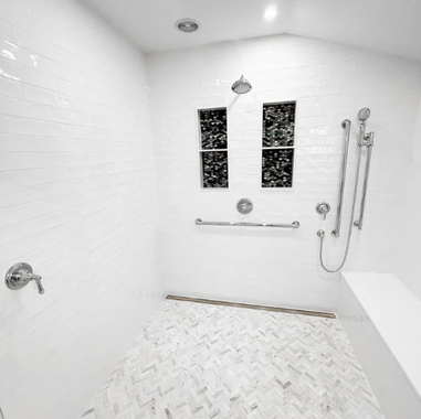 Bright white walk-in shower with bench, grab bars, handheld sprayer, and tiled floor.