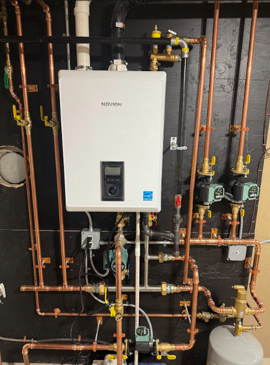 Wall-mounted furnace with exposed pipes and wiring in a utility room.