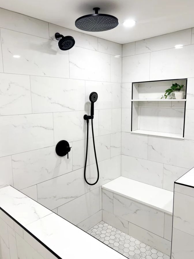 Modern white-tiled shower with black fixtures, built-in bench, shelf niche, and mosaic floor.