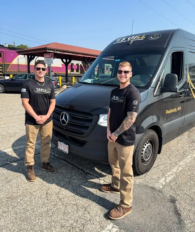 Two men in black shirts and tan pants stand beside a black Mercedes van in a sunny parking lot.