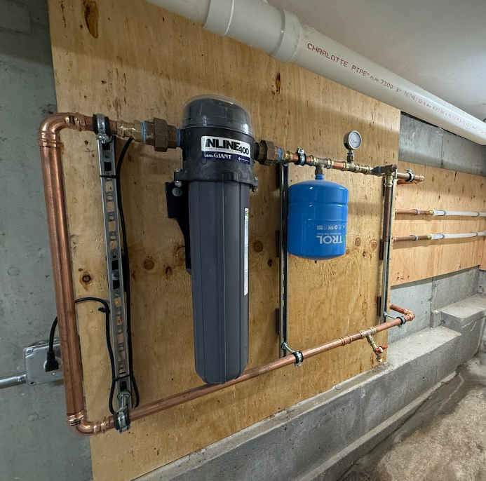 Wall-mounted water filtration system with black and blue canisters and copper pipes in a utility room