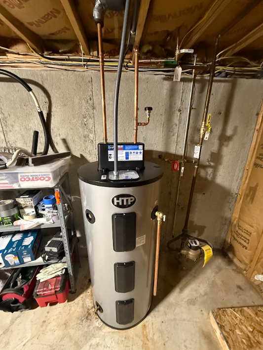 Basement water heater with control panel, exposed pipes, and utility clutter around it