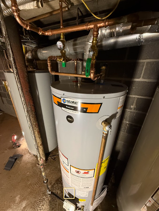 Water heater in a utility closet with exposed pipes and ductwork above it.