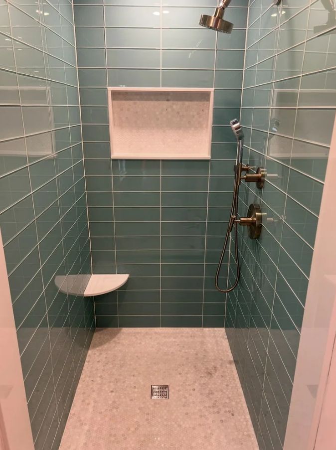 Empty teal-tiled shower stall with built-in bench, shelf, and multiple shower fixtures