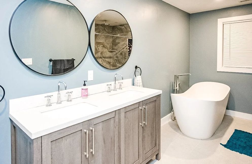 Modern bathroom with double vanity, round mirrors, freestanding tub, and teal rug.