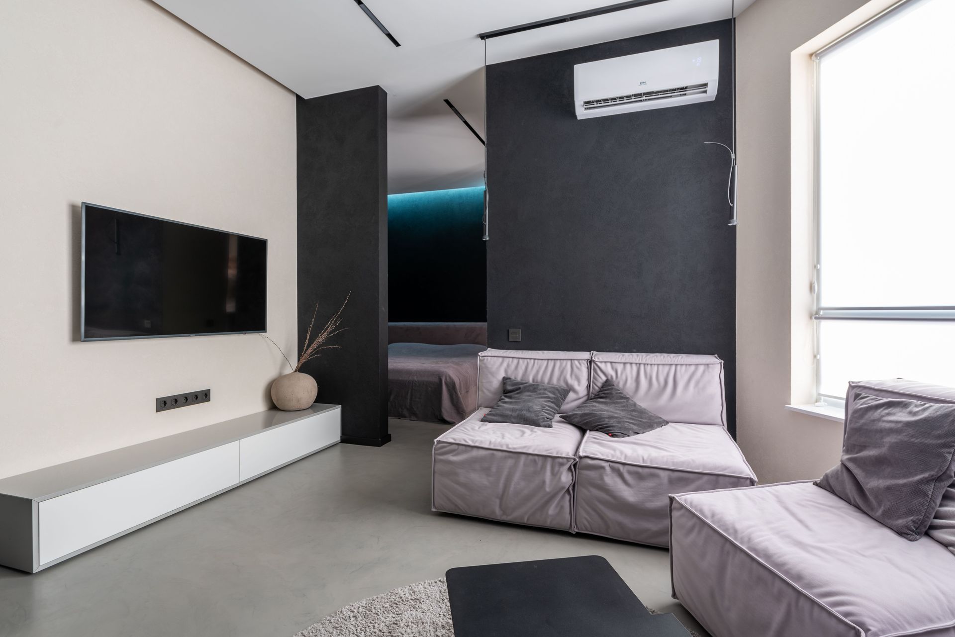 Modern living room with a wall-mounted TV, gray sofa, and minimalist black-and-white decor