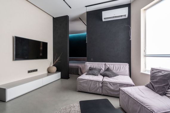 Modern living room with wall-mounted TV, gray sofa, white console, and bright window light