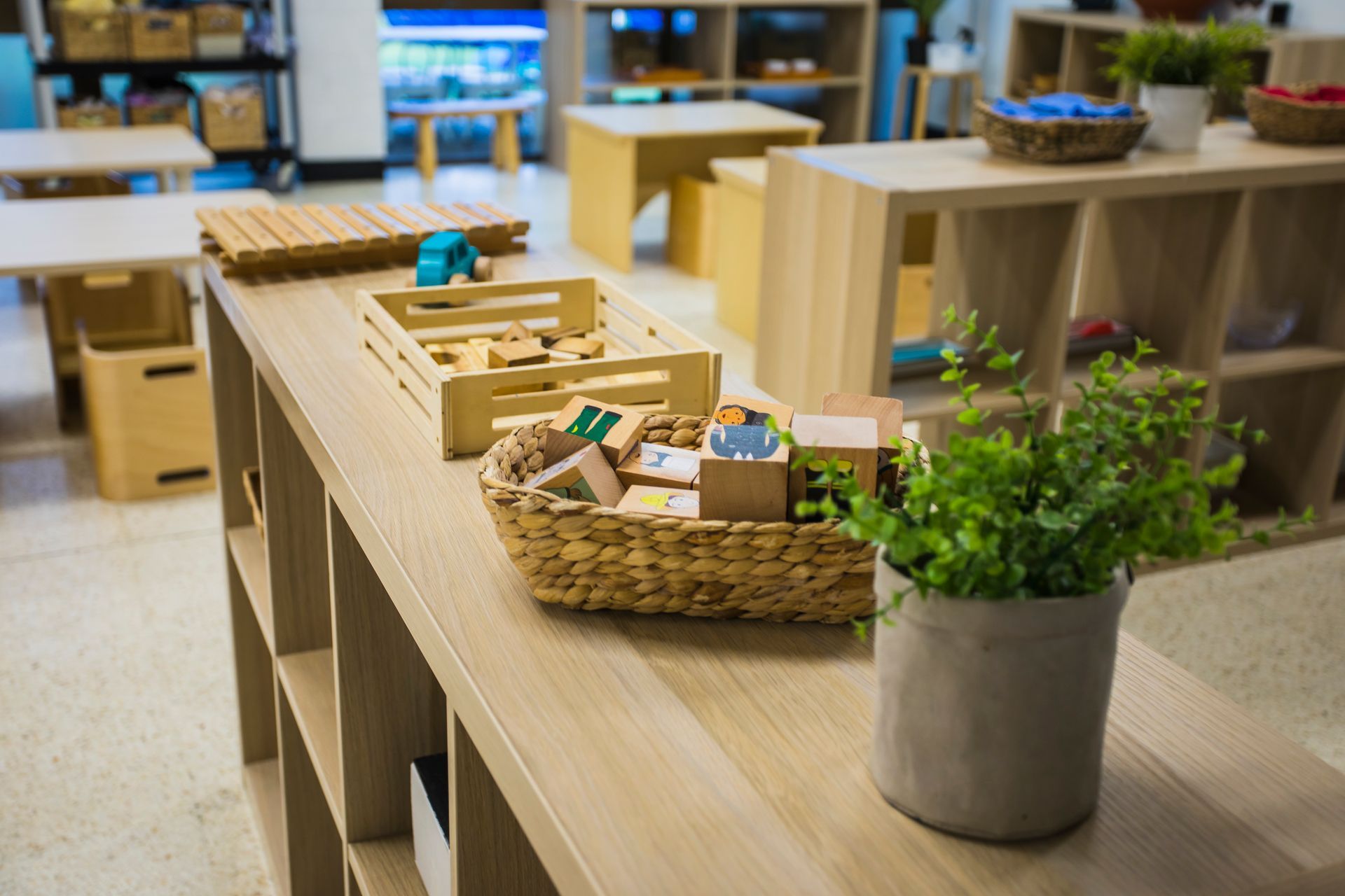 A wooden table with a basket of wooden blocks and a potted plant on it.