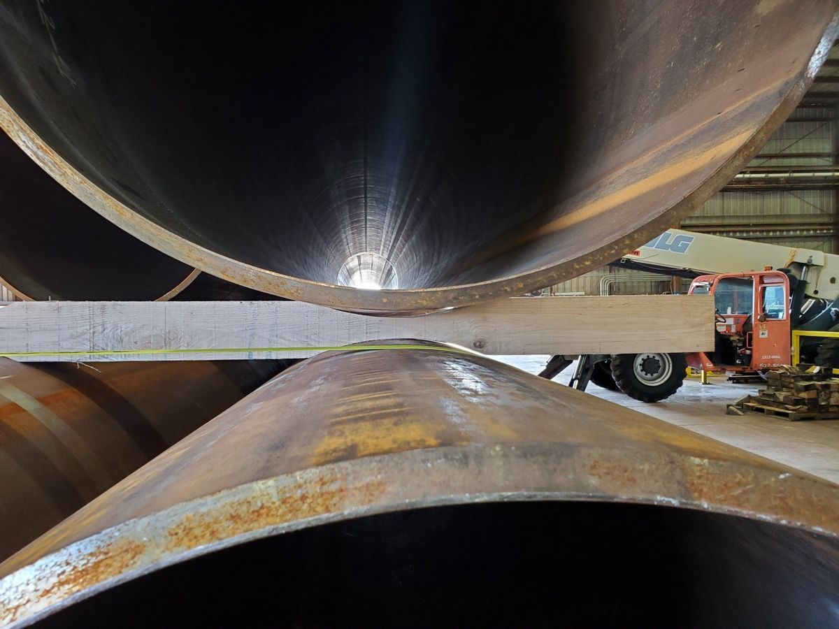 A bunch of metal pipes are stacked on top of each other in a warehouse.