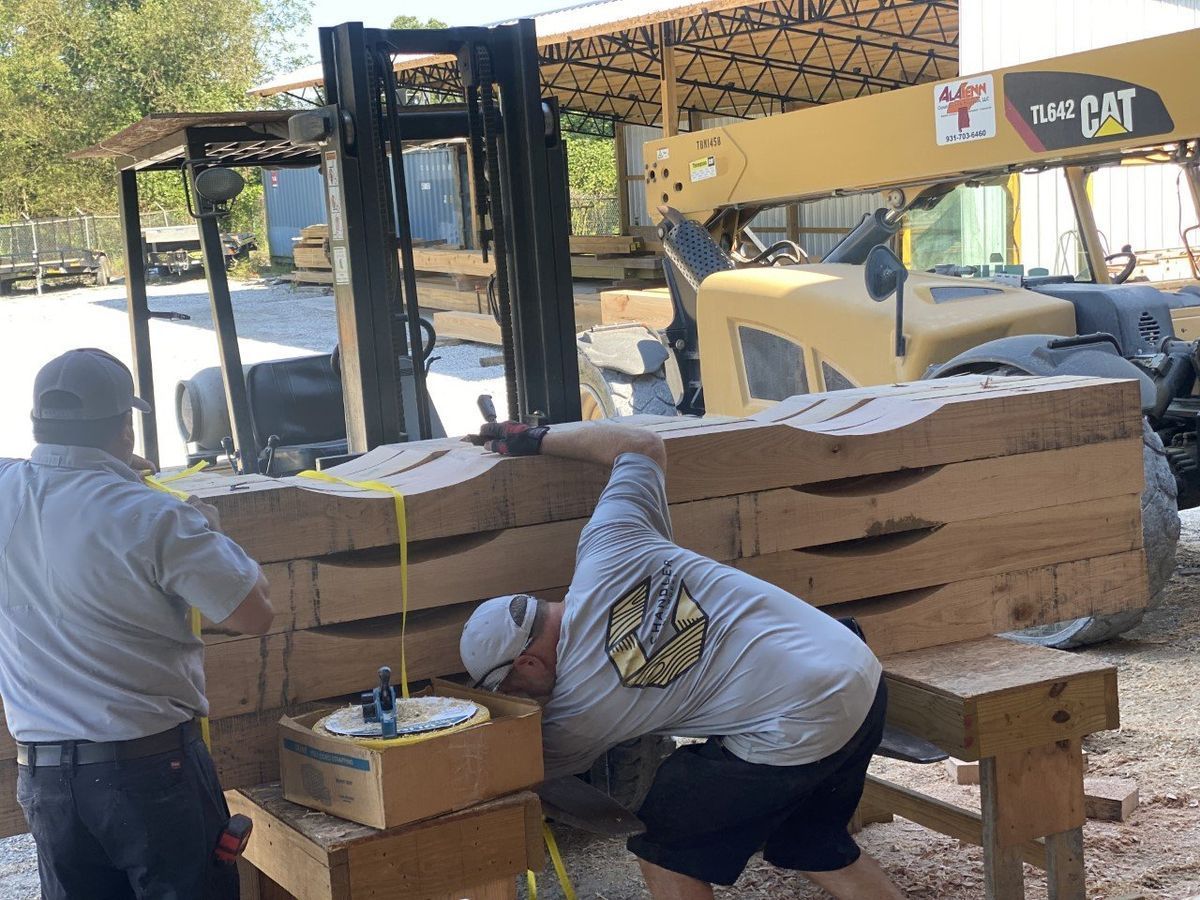 Two men are working on a piece of wood in front of a forklift.