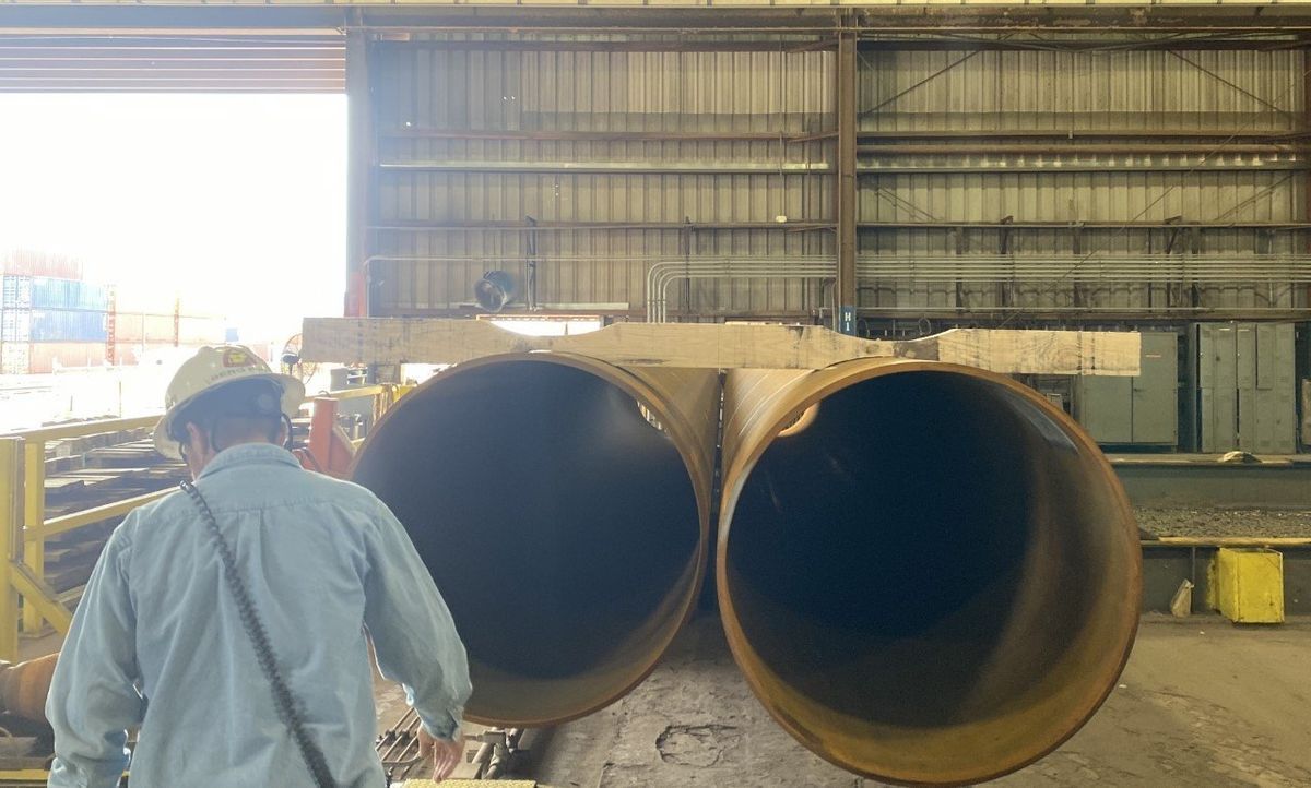 A man is standing next to two large pipes in a warehouse.