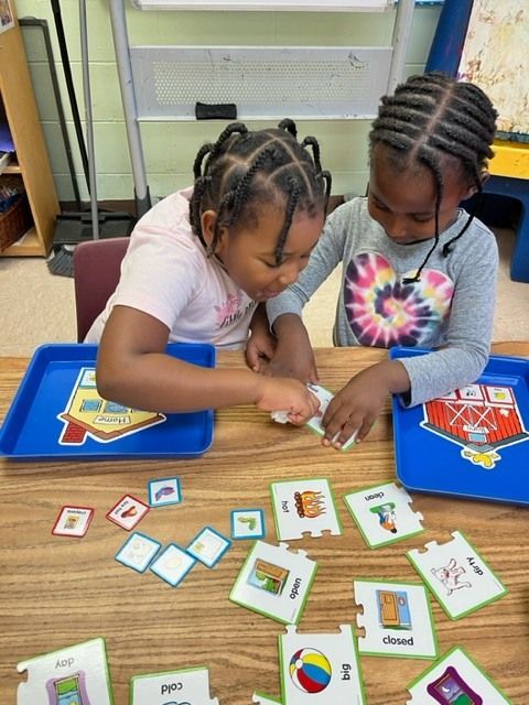 Two young girls are sitting at a table playing with puzzles
