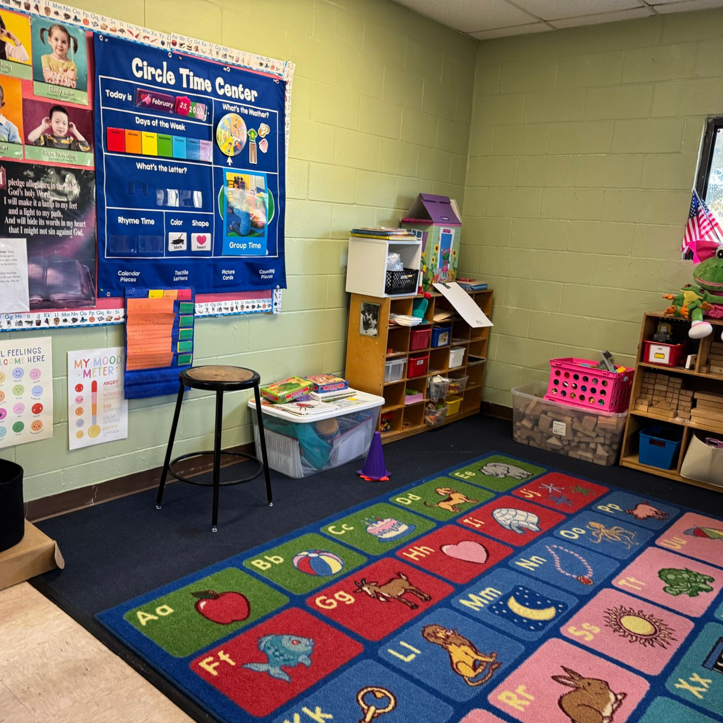 A classroom with a table , chairs , and a rug.