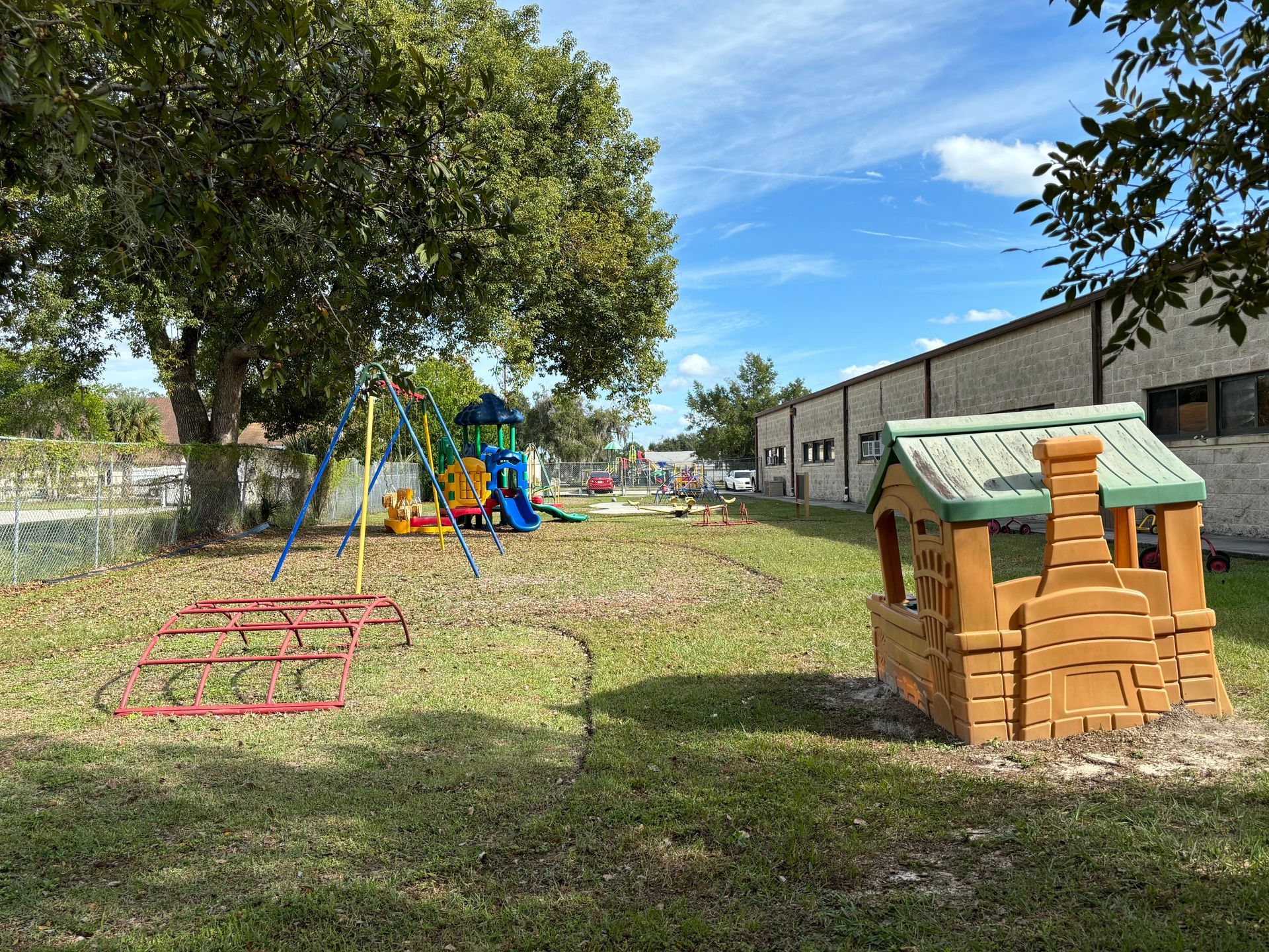 A small playhouse is sitting in the middle of a grassy field next to a playground.