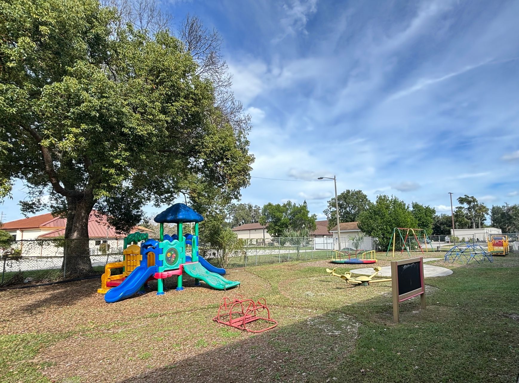 A colorful playground in a park with a chalkboard in the foreground.