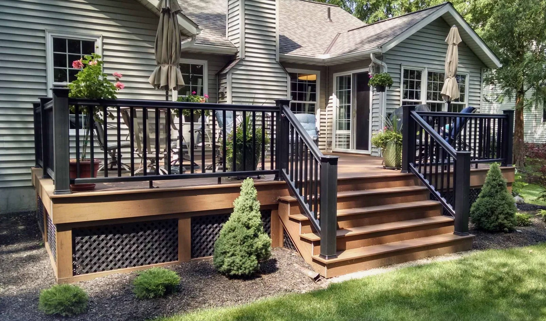 Front porch deck with black railings, wooden steps, and potted plants on a suburban house.