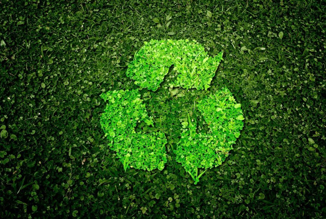 Groen recyclingsymbool van bladeren, geplaatst op gras.