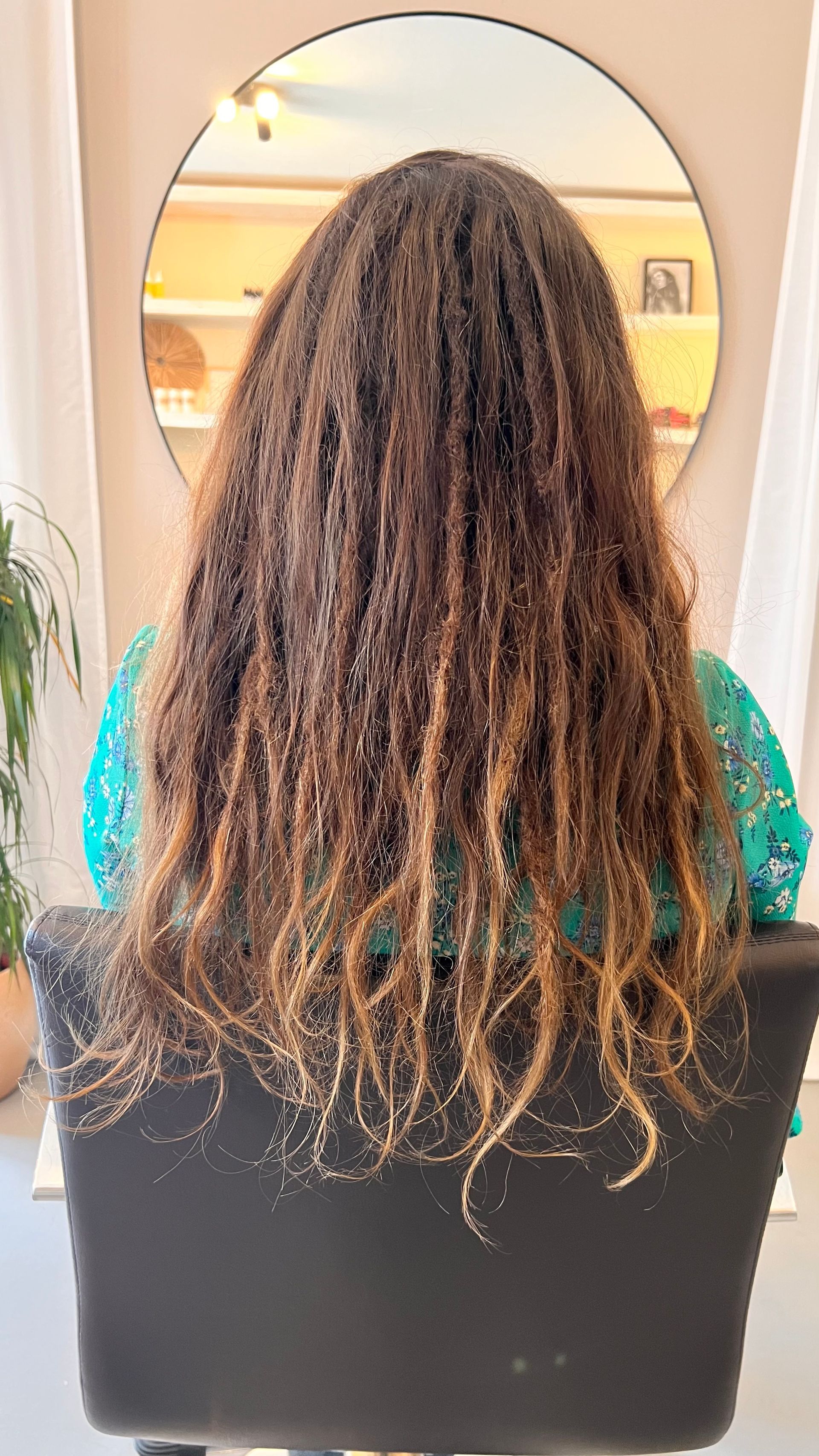 Vrouw met lang, golvend bruin haar zit in een kappersstoel voor een spiegel.