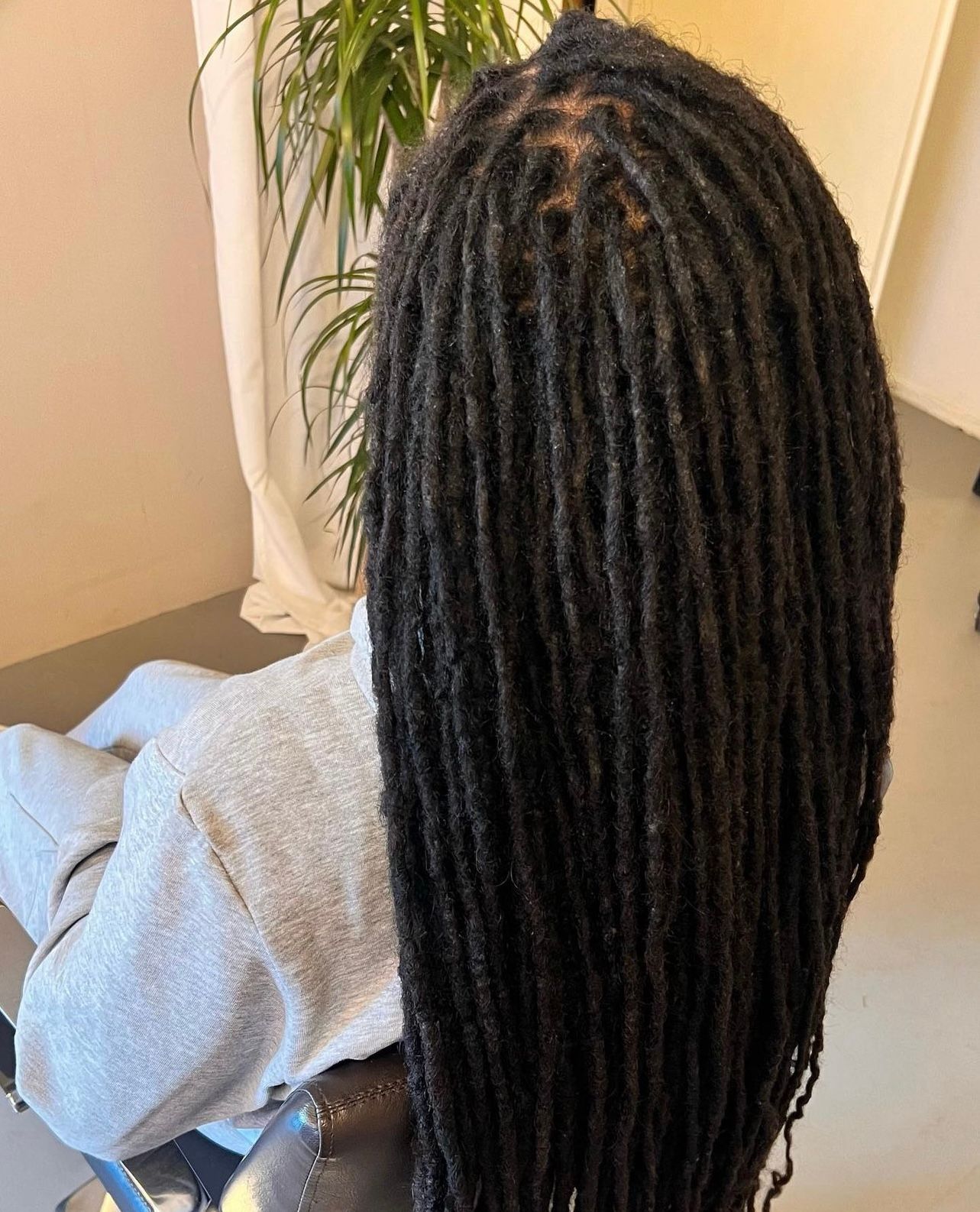 Persoon met lange zwarte dreadlocks, zittend binnen, van achteren gezien.